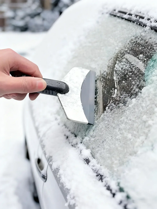 A person using a Grattoir à Glace & Brosse à Neige Universel to clear snow from a car windshield.